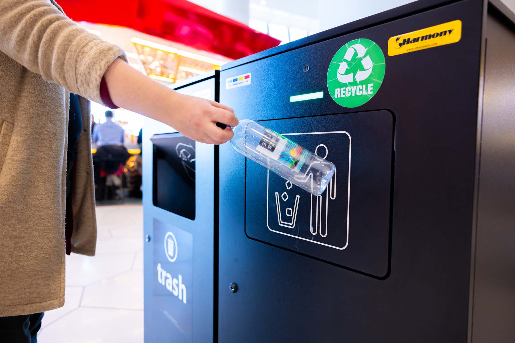 A person throws away a plastic bottle in a recycling receptacle.