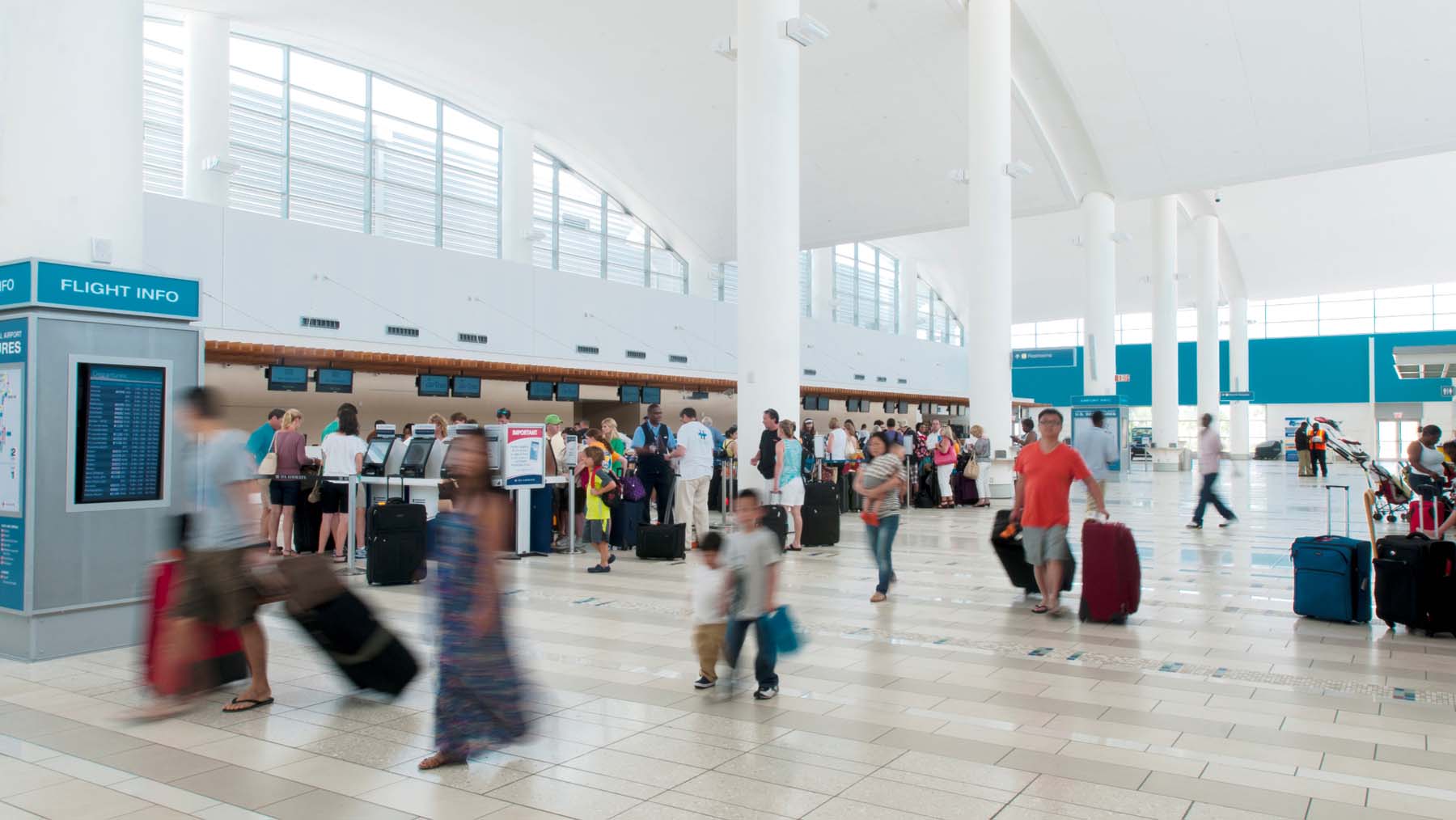 A lot of travelers walk past the check-in counter in an airport terminal.