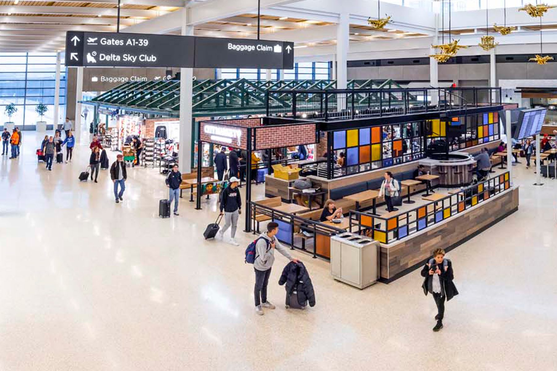 An overhead view of a terminal, showing travelers, gate signs, and retail shops.