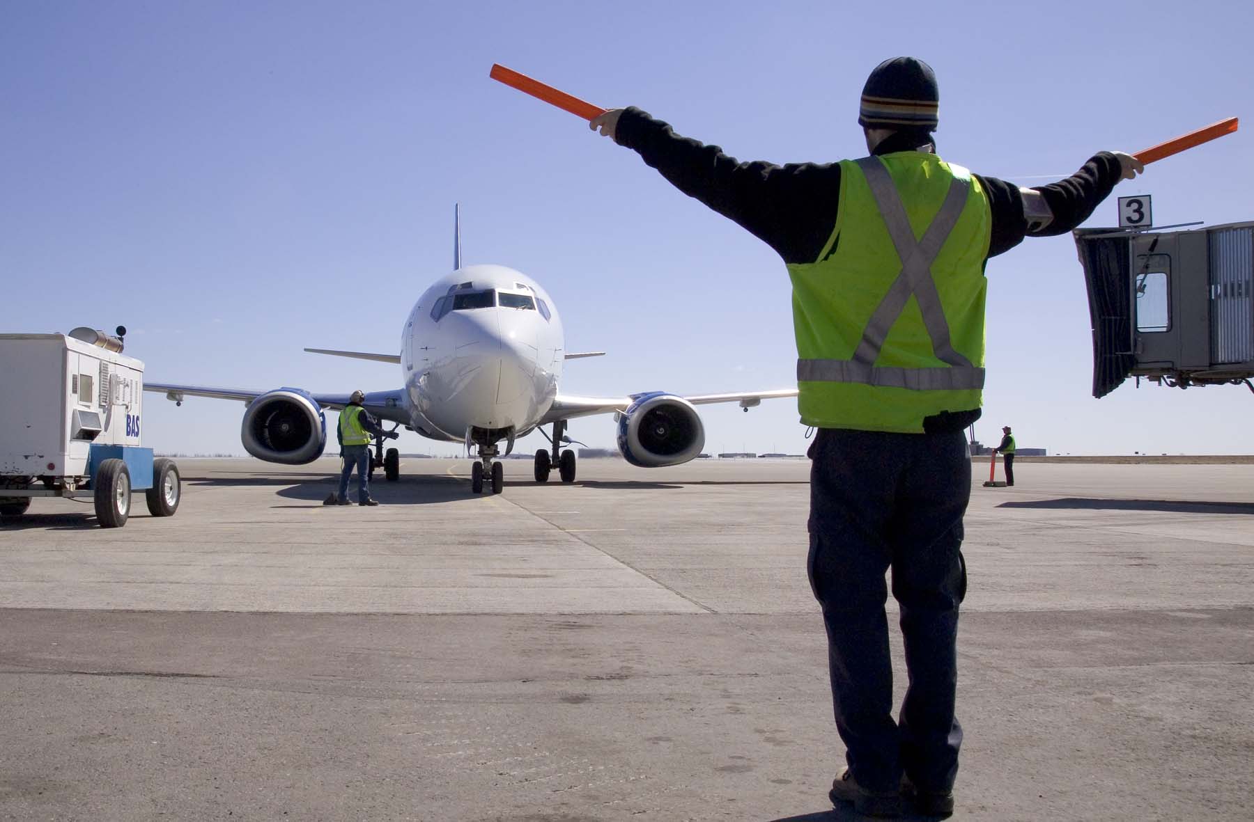 A ground control technician is guiding a mid-sized plane into its terminal gate.