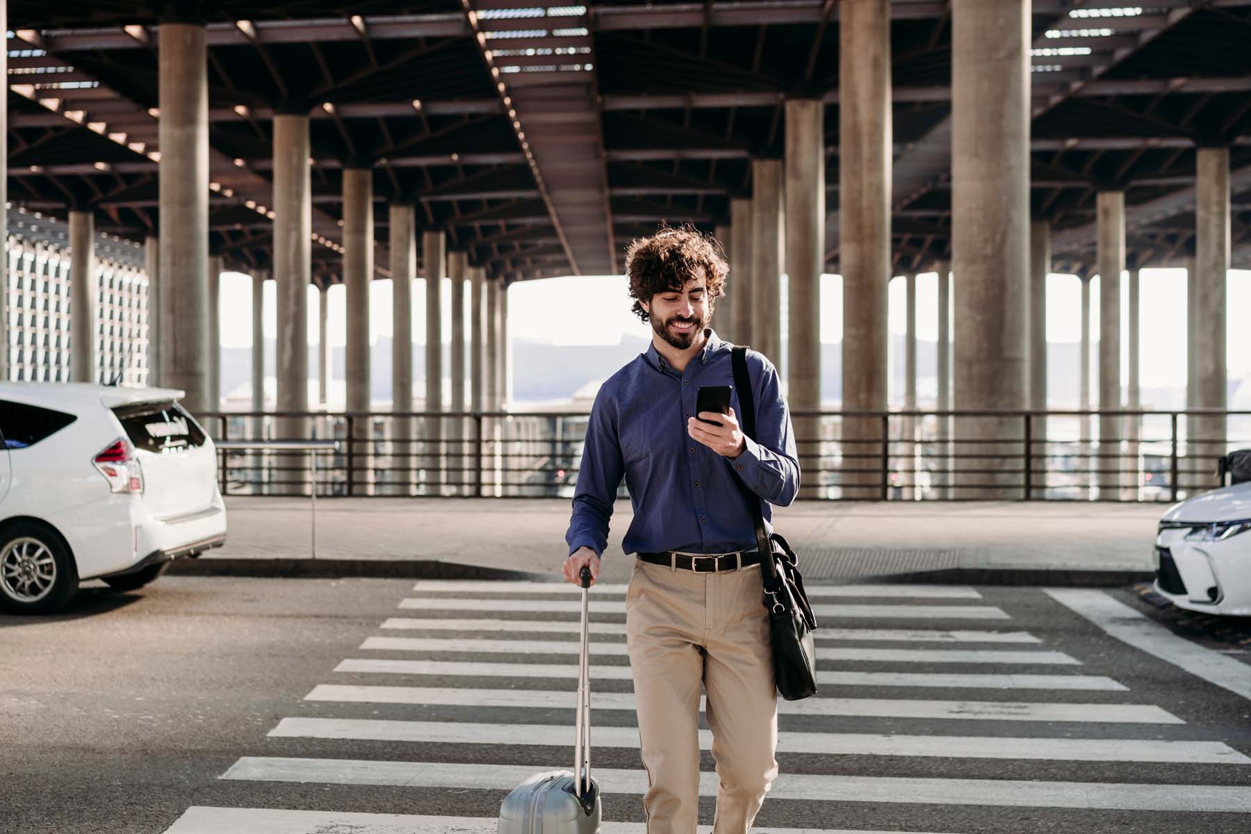 A man walks into an airport terminal while smiling and looking at his smart phone.