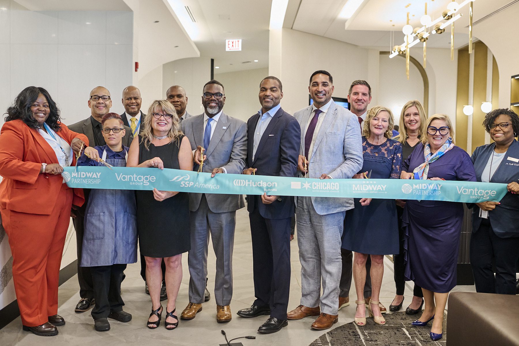 A group of people, many in business attire, stand together holding a large ribbon for a ribbon-cutting ceremony in a modern indoor space. For opening of airport lounge