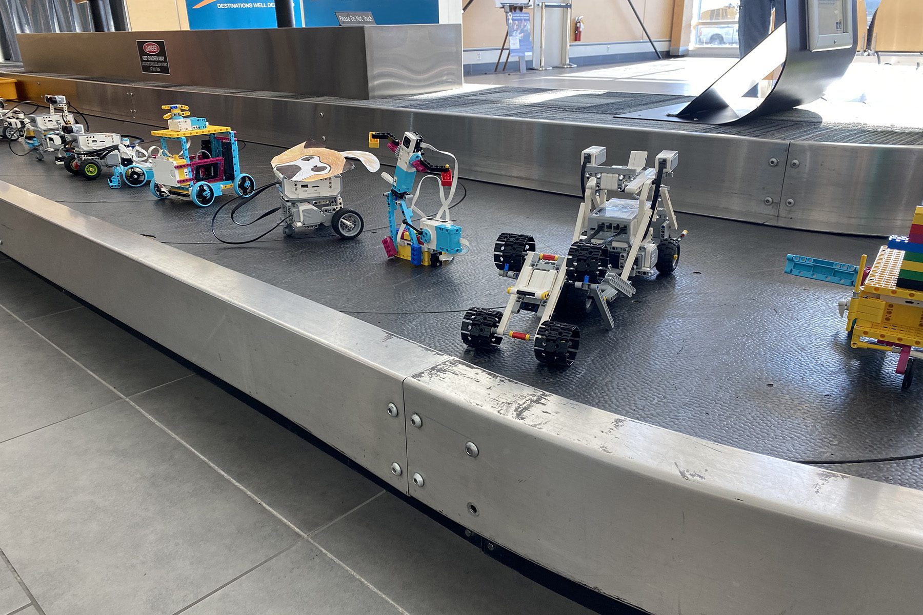 A variety of colorful robot models made from building blocks are displayed on a baggage carousel.