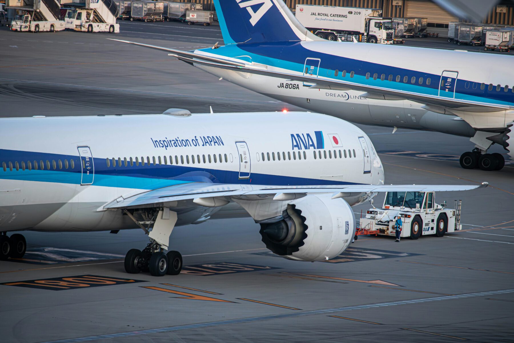 Two ANA airplanes are on the tarmac. One is being towed by a vehicle, while the other is taxiing nearby.