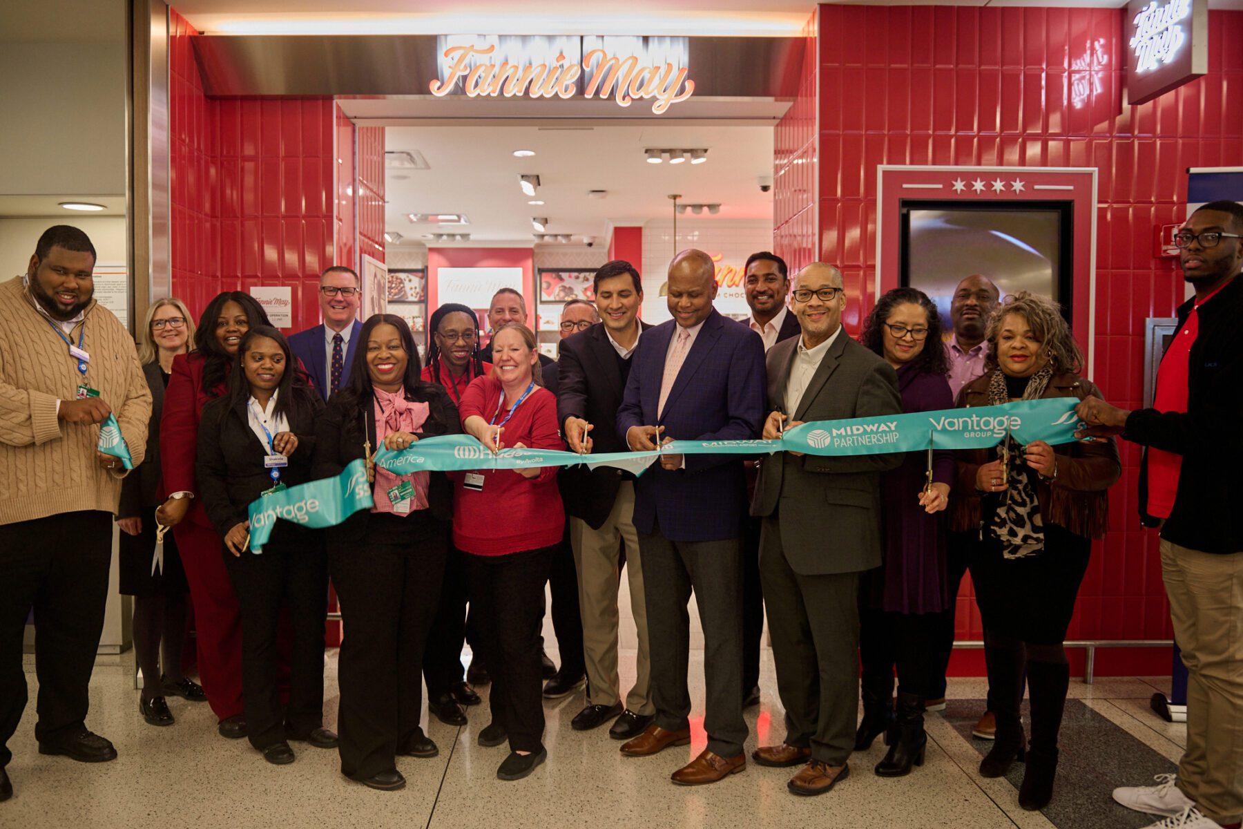 Group of people cutting a ceremonial ribbon with "Midway Partnership" and "Vantage" printed on it, in front of a store entrance.